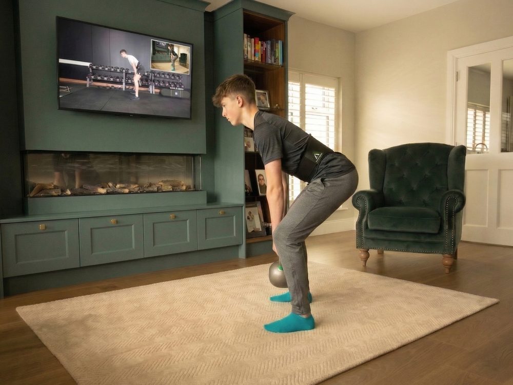 A young man hinged forward over a kettlebell in a green-panelled room, the belt at his waist.